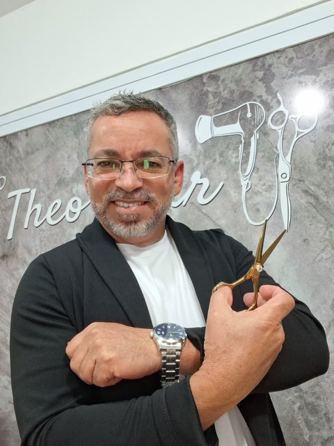 Theo, cabeleireiro e dono do Theo Hair Studio, segurando uma tesoura dourada