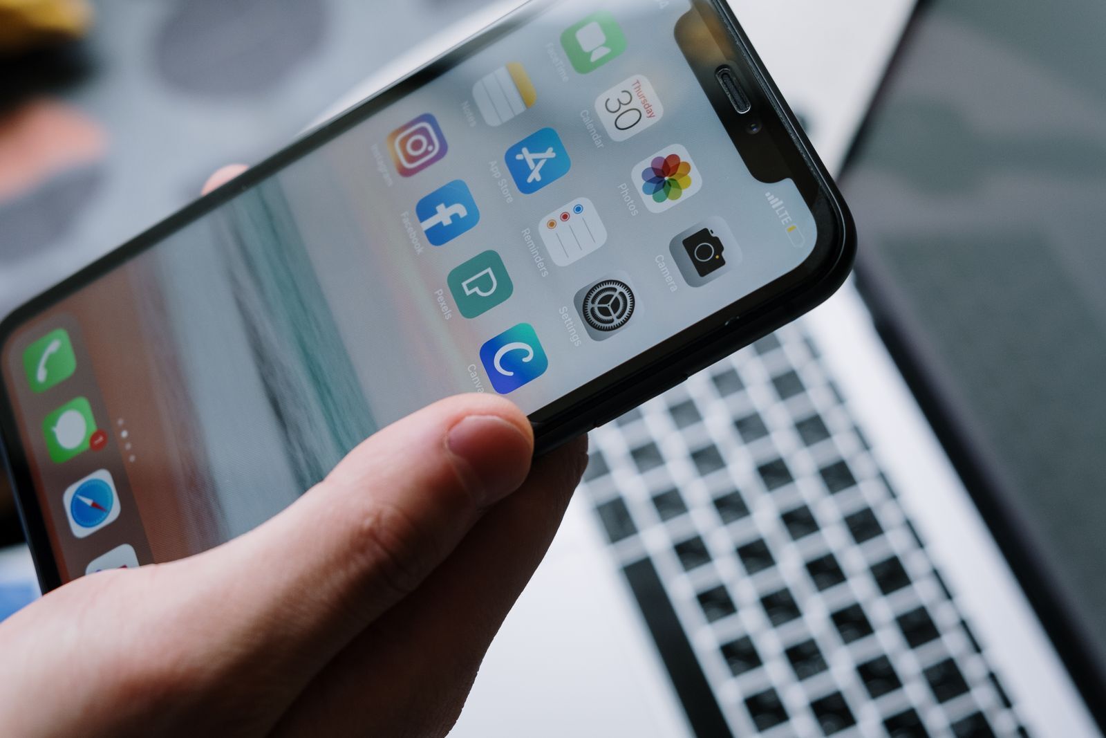 Pessoa com um smartphone na mão diante de um notebook com aplicativos abertos